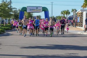 Image of runners at the 2nd Annual Pink Tutu 5K. Several runners wearing pink attire with the blow up start finish line behind them.
